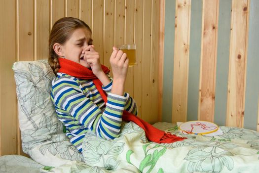 Girl sneezes while sitting in bed with a cup of hot tea