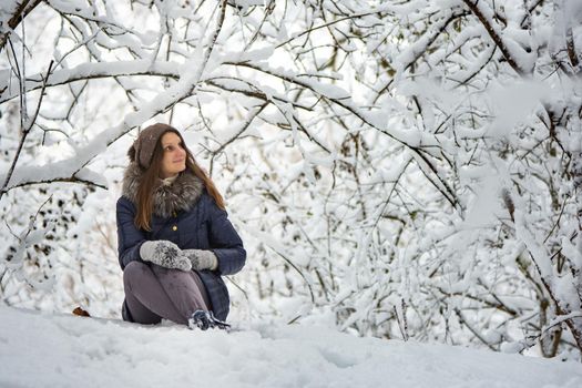 The girl sat down in a beautiful snowy forest and admires the beauty