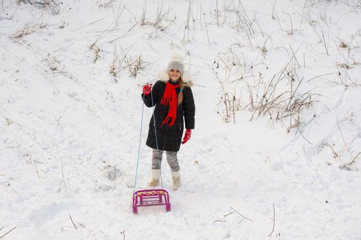 A girl with a sled stands in a snowy meadow