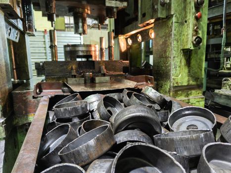pile of stamped thick sheet black metal round parts after a hood operation in front of old blurred forming press with die tooling