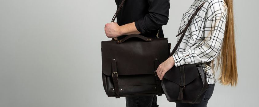 Brown men's shoulder leather bag for a documents and laptop holds by man in a black shirt and woman with a black small bag. Style, retro, fashion, vintage and elegance
