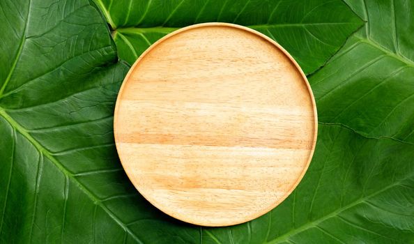 Empty wooden plate on taro leaves background. Top view