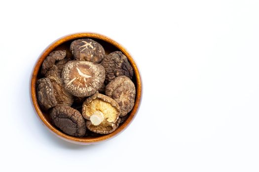 Dried shiitake mushrooms in wooden bowl on white background.