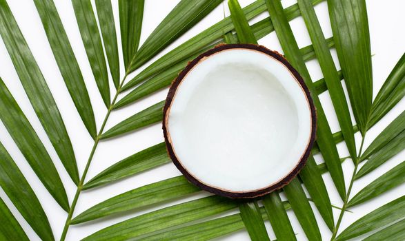 Half coconut on tropical palm leaves on white background. Top view