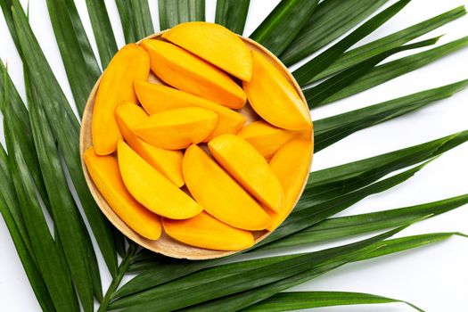 Mango slices on wooden plate on tropical palm leaves.