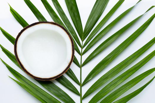 Half coconut on tropical palm leaves on white background. Top view