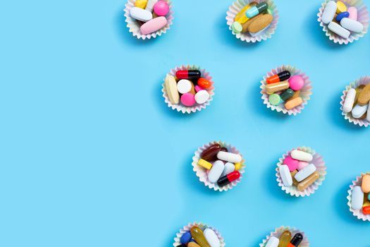 Colorful tablets with capsules and pills in cupcake wrappers on blue background.