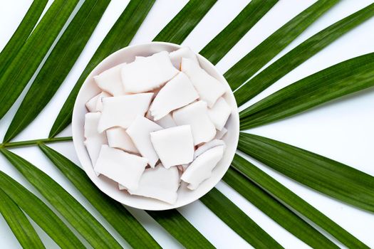 Coconut pieces on dish plate on tropical palm leaves. Top view
