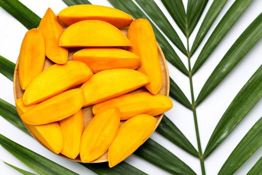 Mango slices on wooden plate on tropical palm leaves. Top view