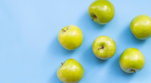 Green apples on blue background. Copy space