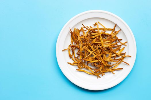 Dried Lily Buds on white plate on blue background. Copy space