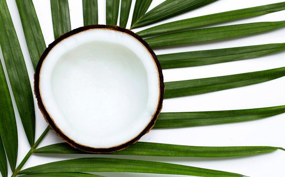Half coconut on tropical palm leaves on white background. Top view