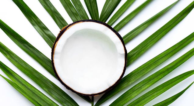 Half coconut on tropical palm leaves on white background. Top view