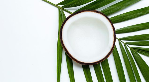 Half coconut on tropical palm leaves on white background. Top view