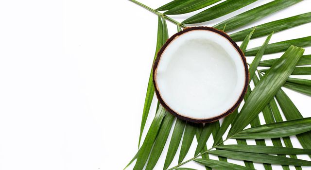 Half coconut on tropical palm leaves on white background. Top view