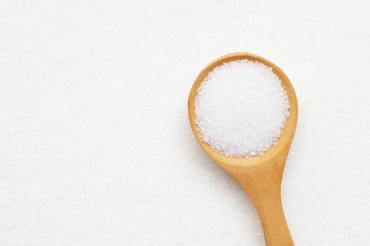 Wooden spoon with white granulated sugar. Top view