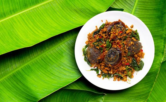 Thai food. Stir-fried minced pork, preserved egg  with basil leaves on banana leaves background.