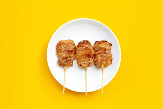 Grilled pork on white plate on yellow background.