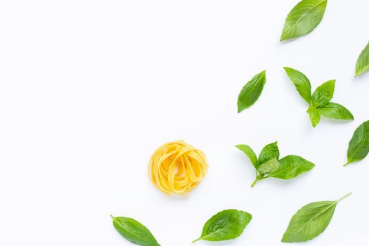 Raw tagliatelle pasta with basil leaves on white background.