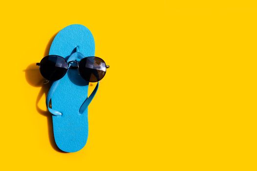 Blue flip flops with sunglasses on yellow background. Enjoy summer holiday concept.