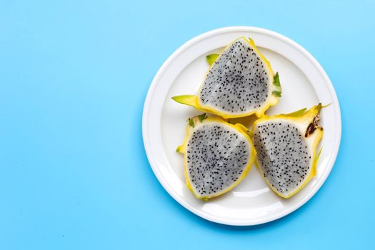 Yellow pitahaya or dragon fruit on white plate on blue background. Copy space