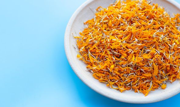 Petals of marigold flower on plate. Blue background with copy space
