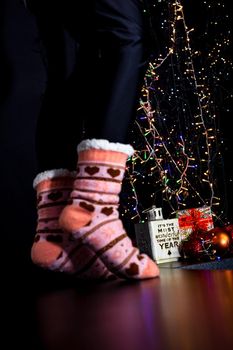 Female legs in Christmas colorful socks near Christmas tree.