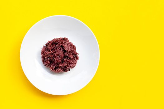 Black sticky rice on white ceramic dish on yellow background. Copy space