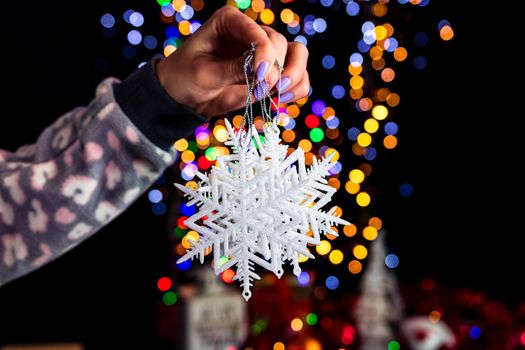 Holding Christmas snowflake decoration isolated on background with blurred lights. December season, Christmas composition.