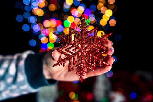 Holding Christmas snowflake decoration isolated on background with blurred lights. December season, Christmas composition.