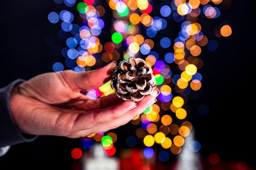 Holding Christmas pine cone decoration isolated on background with blurred lights. December season, Christmas composition.