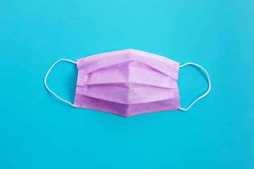 Pink protective medical mask on blue background. Top view