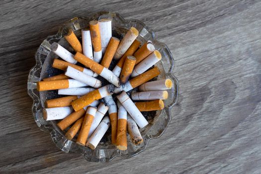 Cigarettes buds in a transparent ashtray on wooden background. Copy space