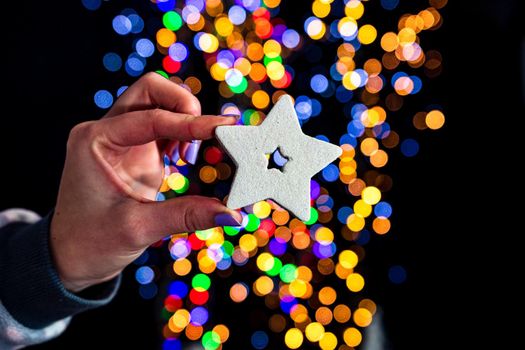 Holding Christmas glittery star decoration isolated on background with blurred lights. December season, Christmas composition.