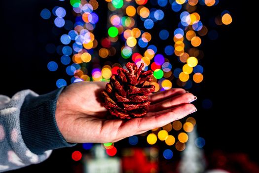 Holding Christmas pine cone decoration isolated on background with blurred lights. December season, Christmas composition.