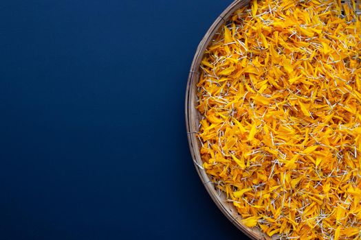 Marigold flower petals in wooden bamboo threshing basket on dark background.