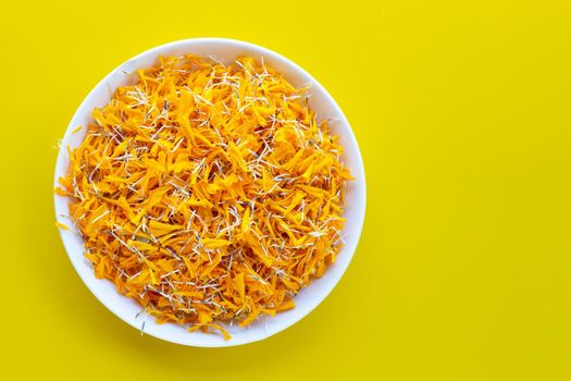 Marigold flower petals in white plate on yellow background.