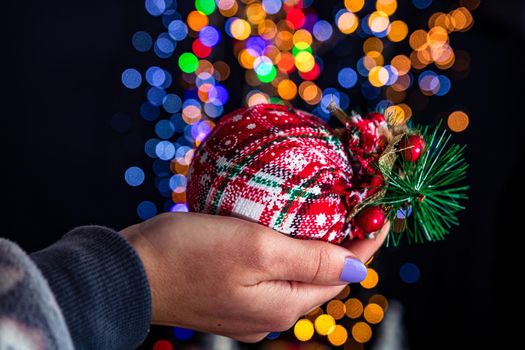 Holding Christmas bauble decoration isolated on background with blurred lights. December season, Christmas composition.