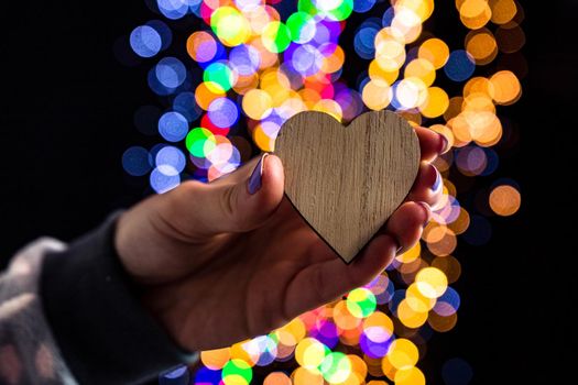 Holding Christmas heart shape decoration isolated on background with blurred lights. December season, Christmas composition.