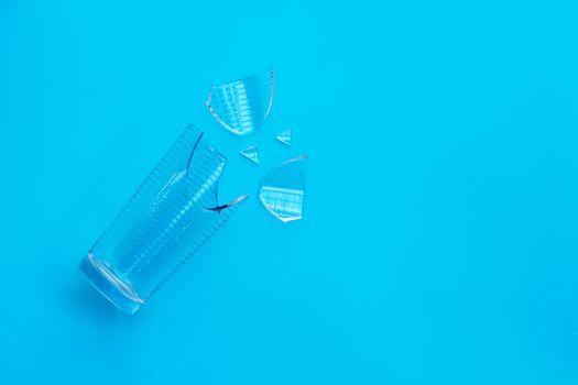 Empty broken drinking glass on blue background. Copy space