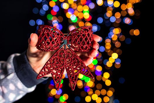 Holding Christmas red ribbon decoration isolated on background with blurred lights. December season, Christmas composition.