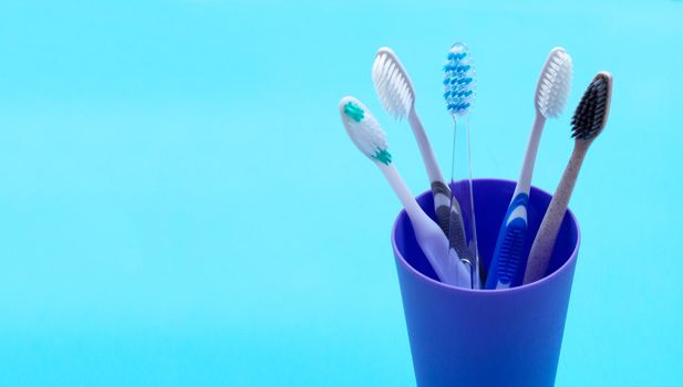 Toothbrushes in plastic glass on blue background. Copy space