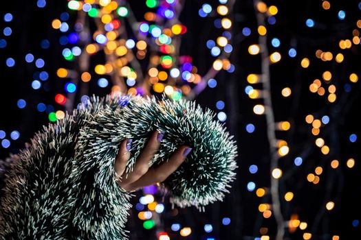 Holding Christmas garland decoration isolated on background with blurred lights. December season, Christmas composition.