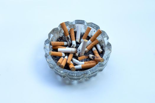 Cigarettes buds in a transparent ashtray on white background.