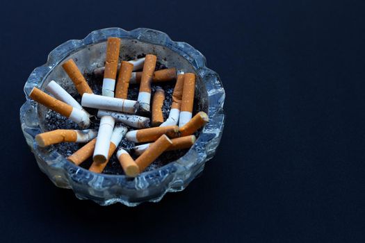 Cigarettes buds in a transparent ashtray on dark background.