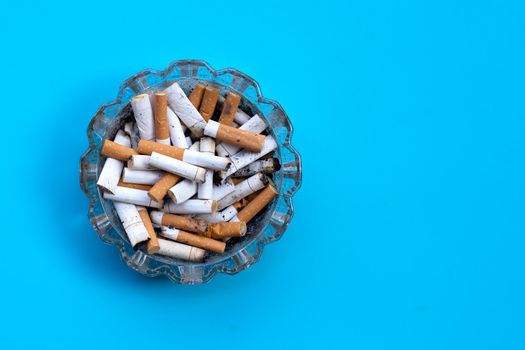 Cigarettes buds in a transparent ashtray on blue background.