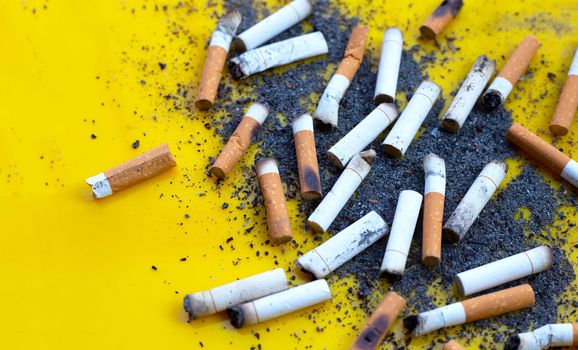 Ashtray and cigarettes on yellow background. 