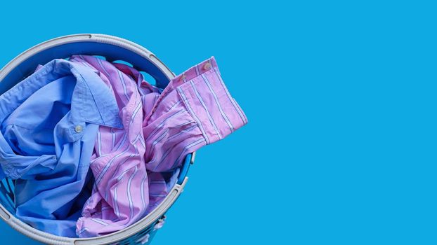 Clothes in a laundry basket on blue background. Copy space