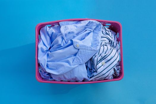 Clothes in a laundry basket on blue background. Copy space