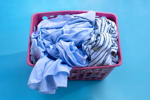 Clothes in a laundry basket on blue background. Copy space